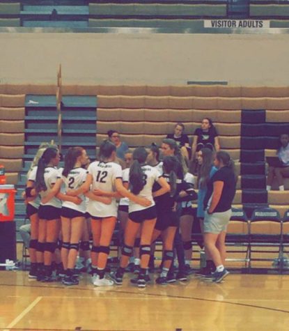 The volleyball team is gathered in a huddle, talking about the next move in the game