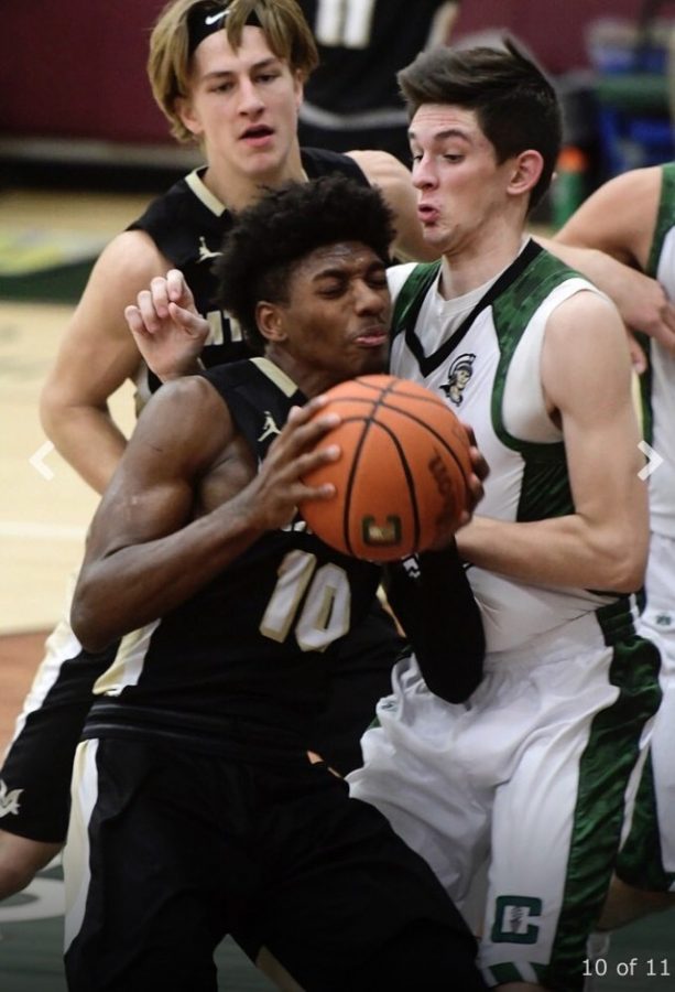 A basketball player is holding the ball to his chest as he defends the ball.