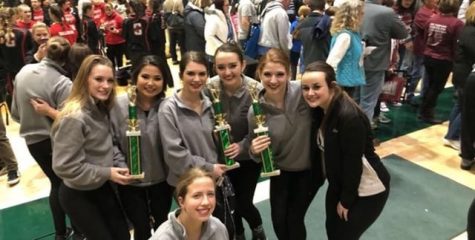 The dance team girls huddle around with their trophies in hand.