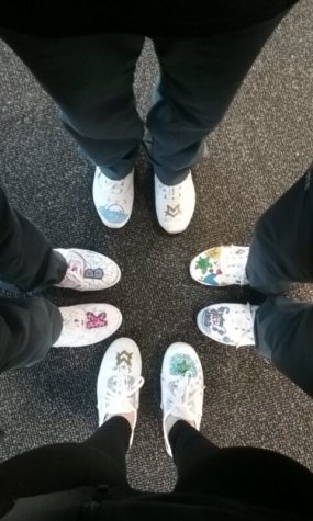 The swim girls are taking a picture of their shoes in a circle, and the shoes are all uniquely decoratedl