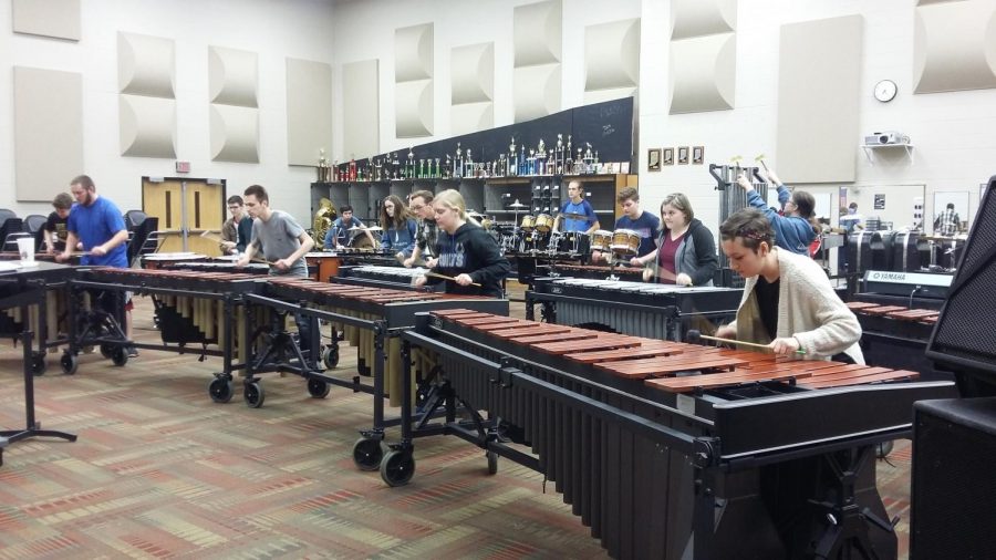 Students play large percussion instruments while sitting in a row.