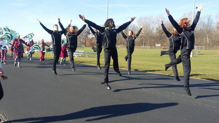 multiple color guard members are leaping into the air with lots of energy excitement