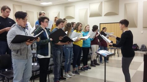 Choir students hold folders of sheet music while practicing.