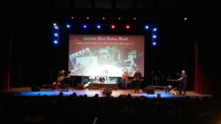 A band stands on a stage ready to perform, with a visual behind them that states "Celebrate Black History Month."