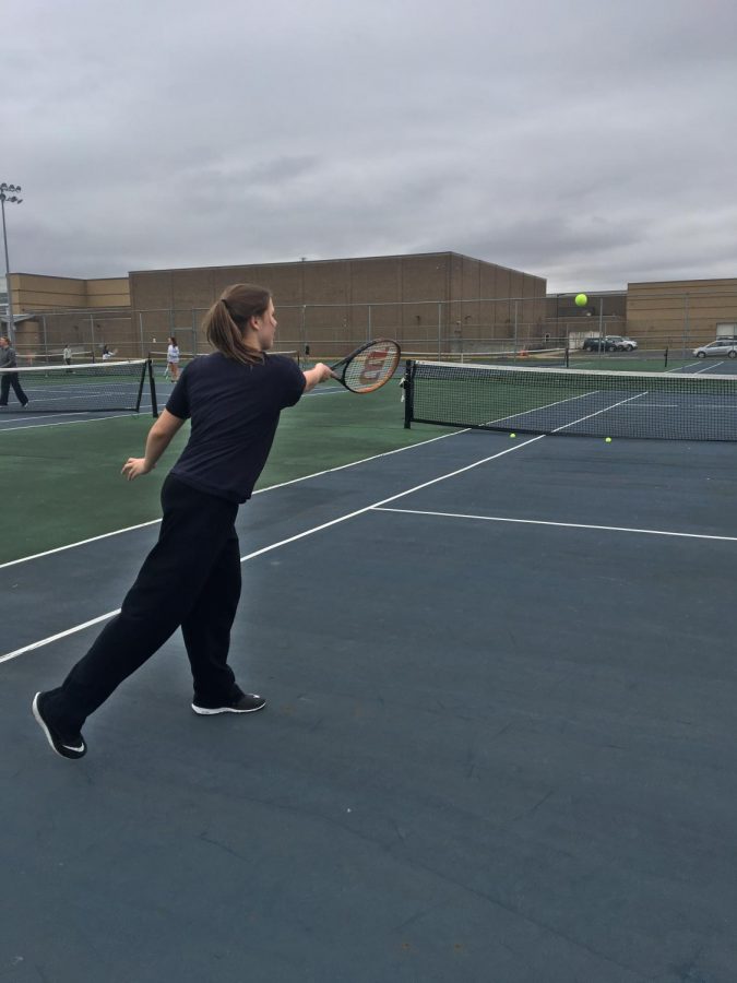 A girl is standing on the court and just hit a tennis ball to the other side of the court.