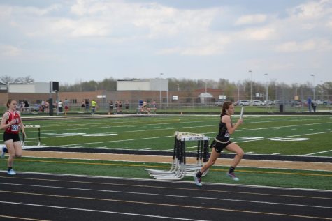 A girl with a baton in her hand runs for first place.