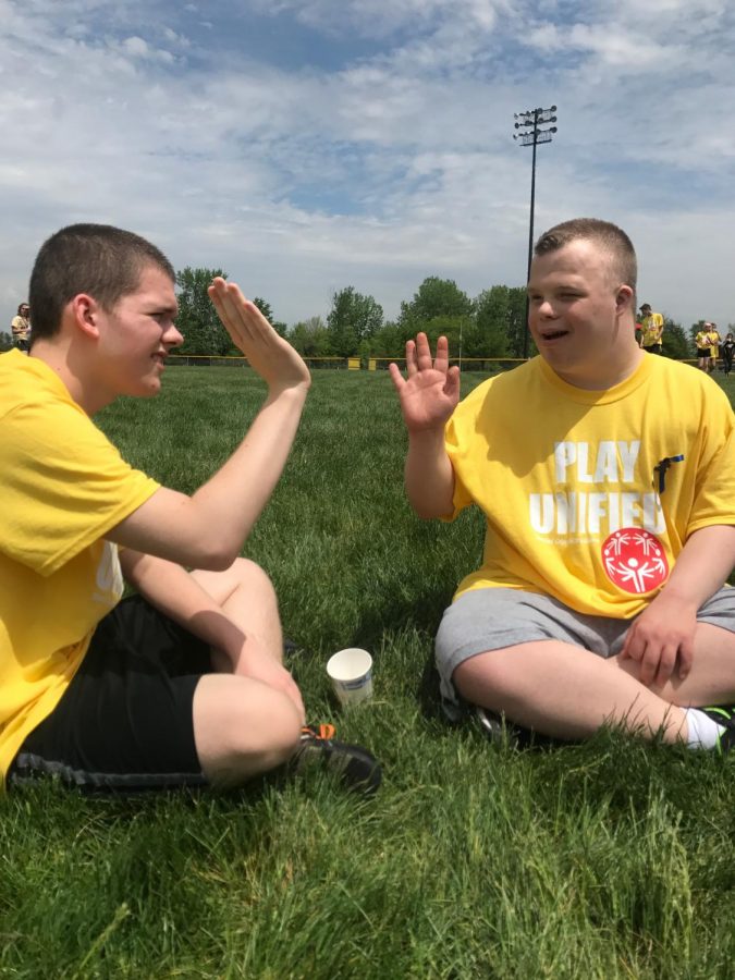 Two boys sit on the ground, high-fiving.